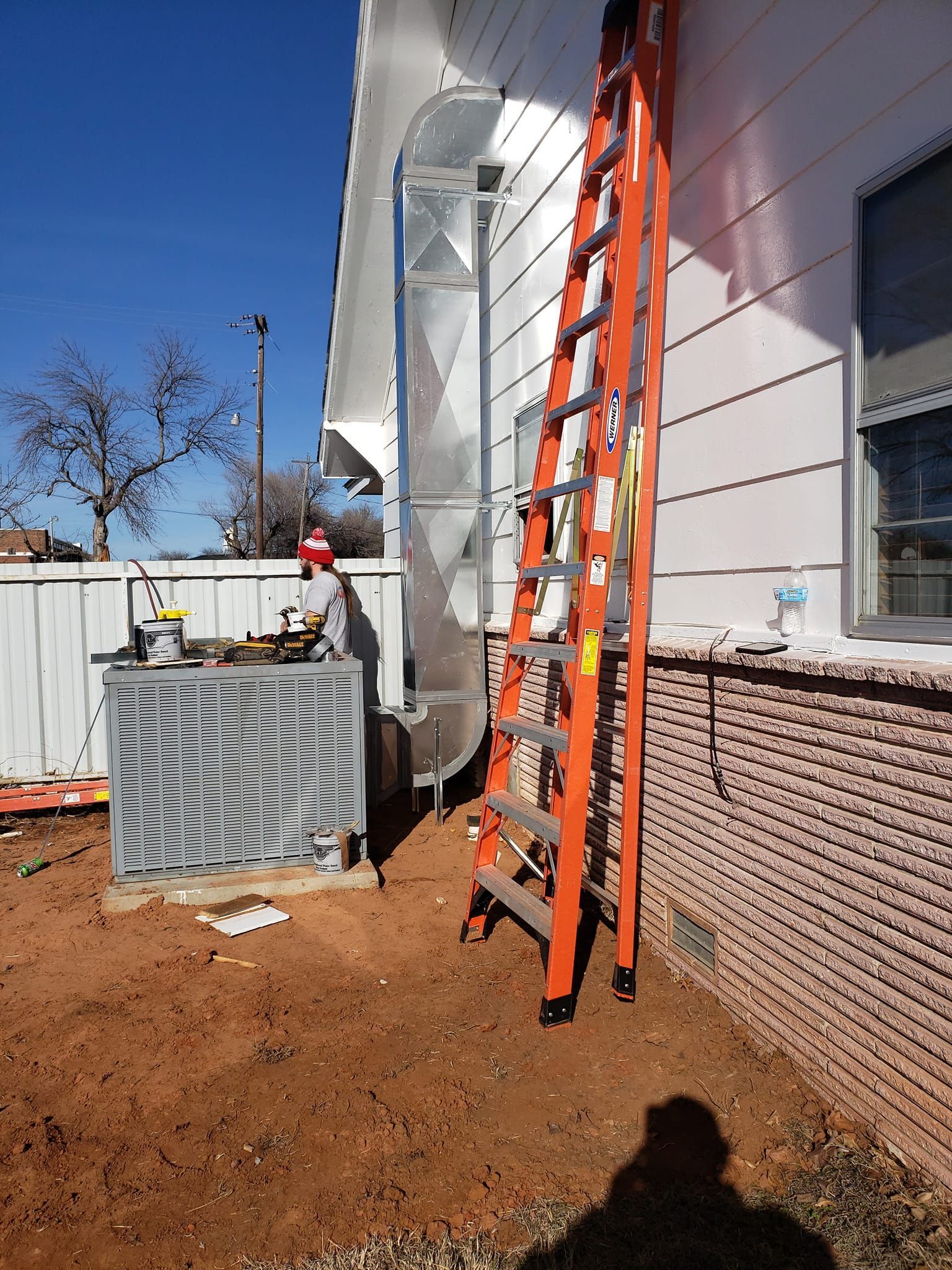 Orange ladder next to a house with a metal air duct. An air conditioning unit is in the foreground.