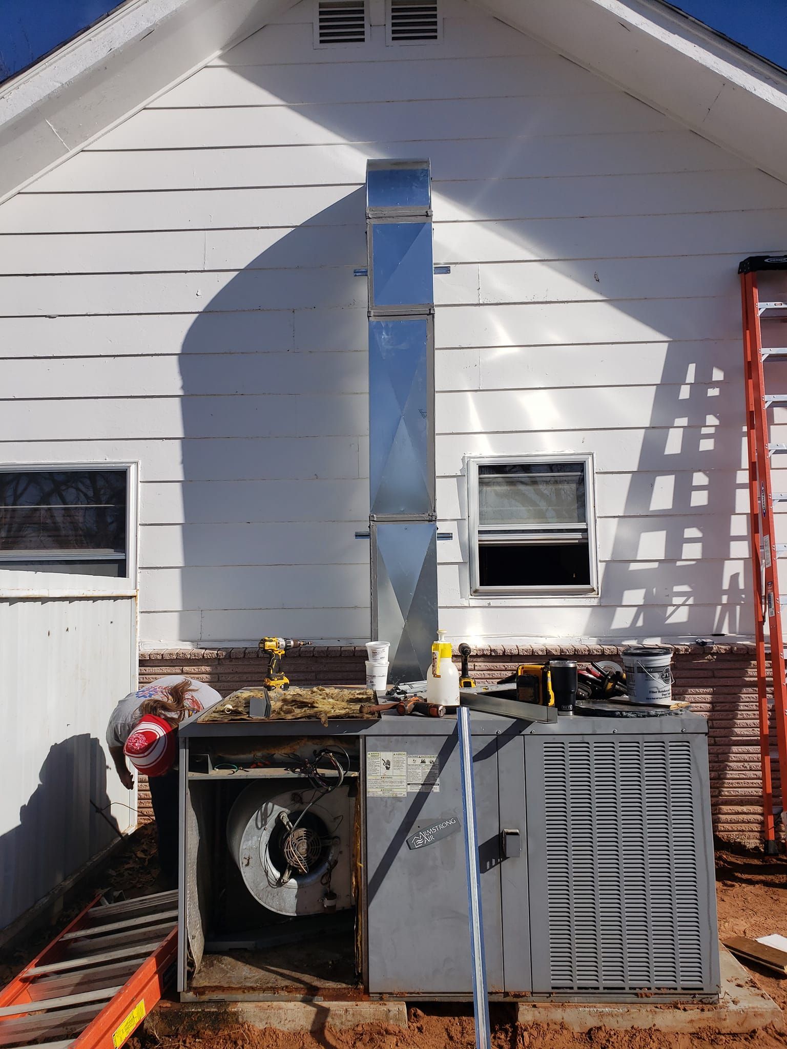 Furnace outside a white building with vent pipe. A person is working on it.