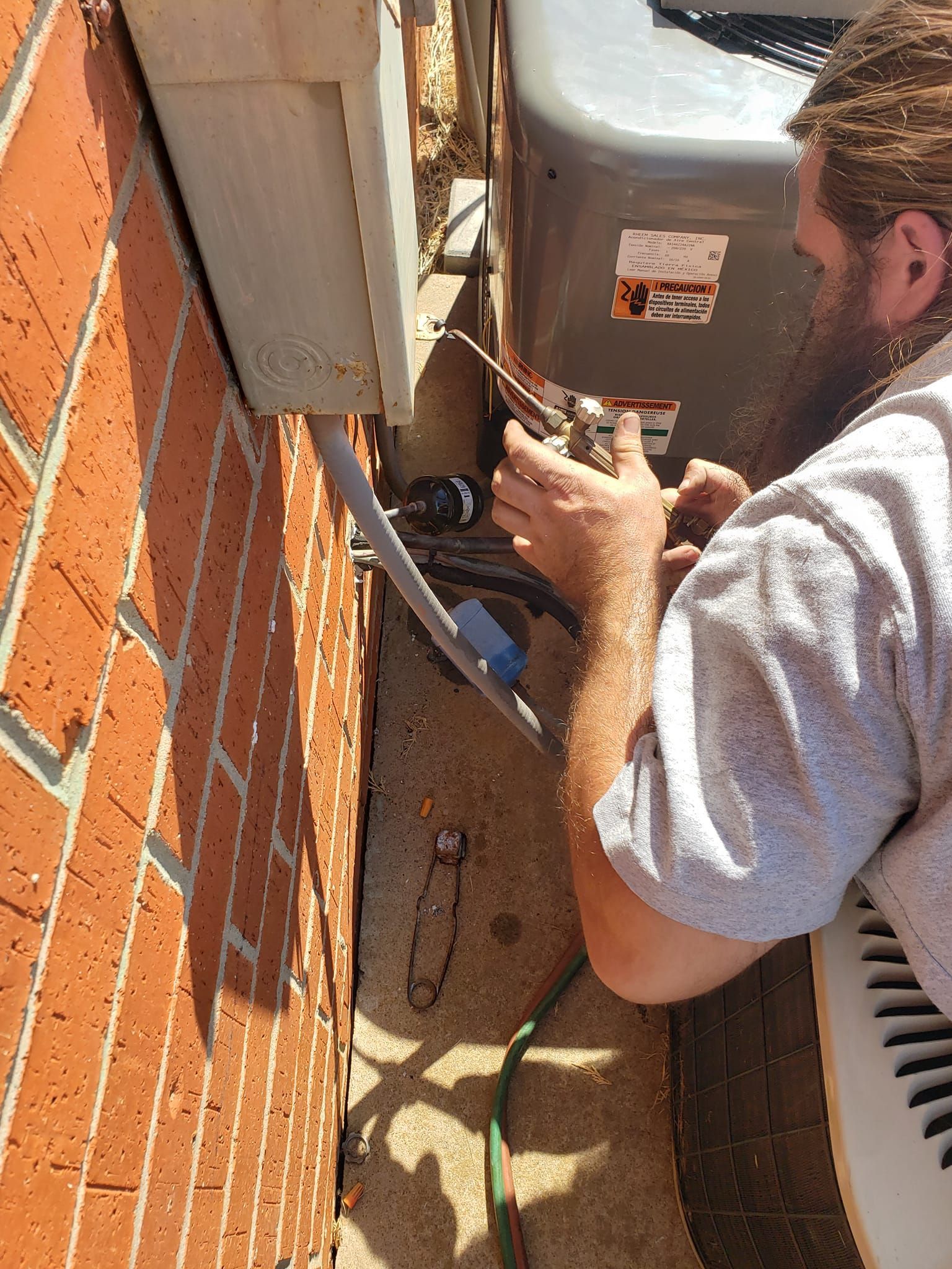 Person working on HVAC unit next to a brick wall.