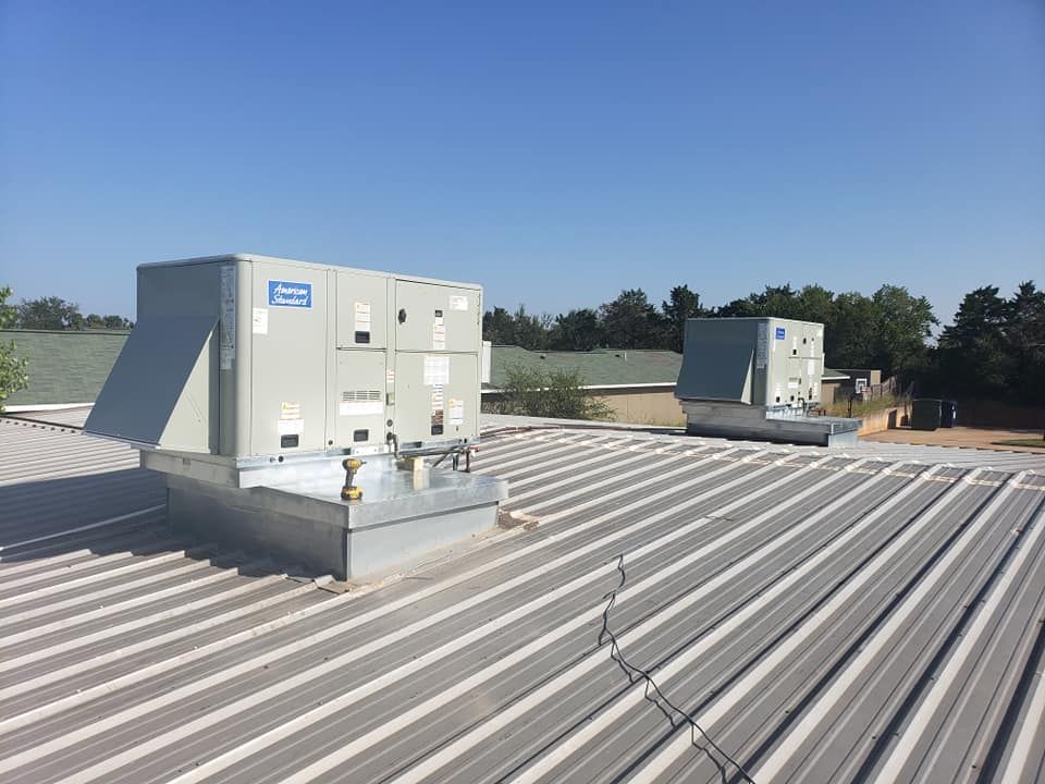 Two rooftop HVAC units on a corrugated metal roof under a blue sky.