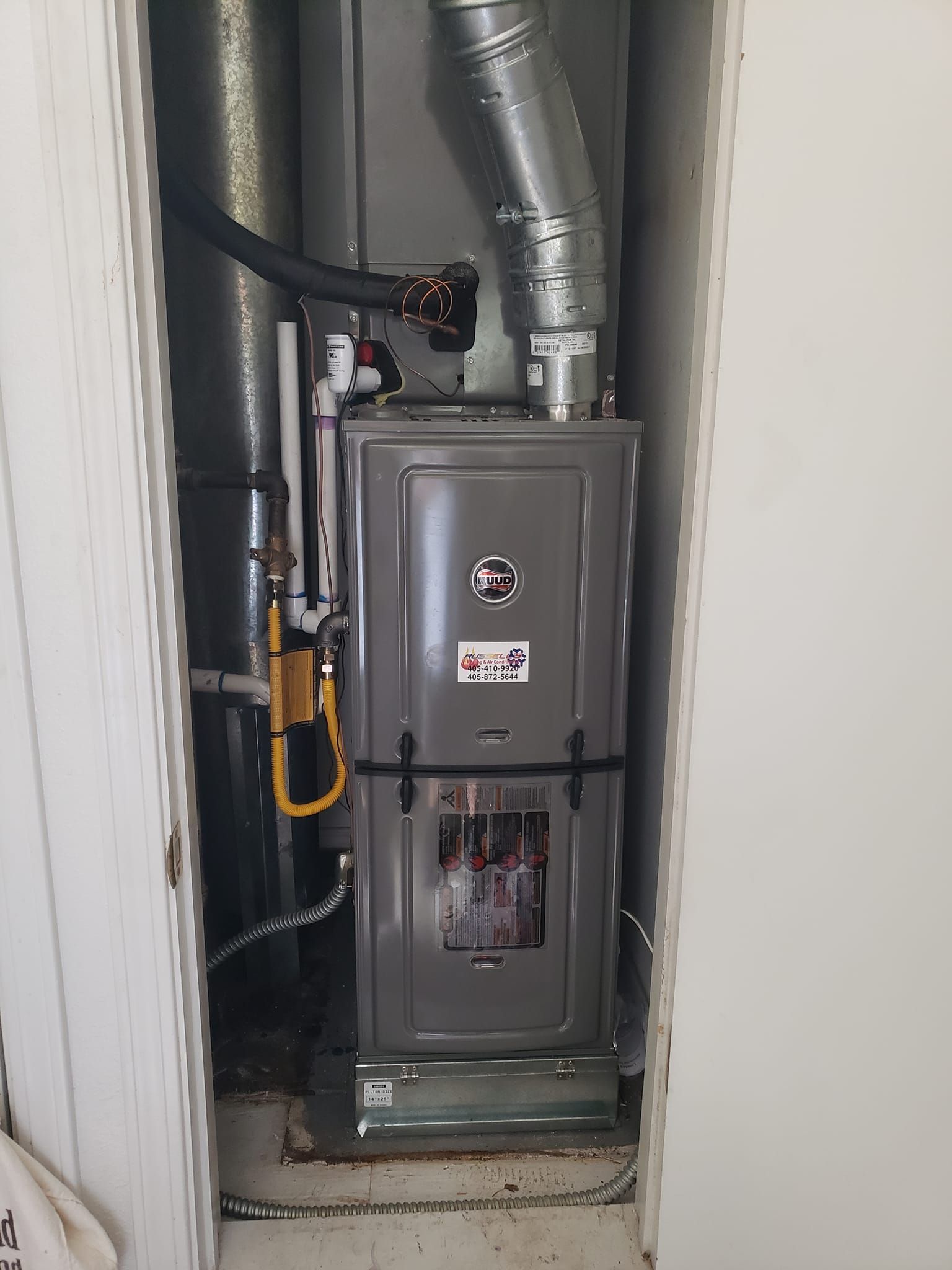 A furnace in a closet, with silver ductwork and gas lines visible.