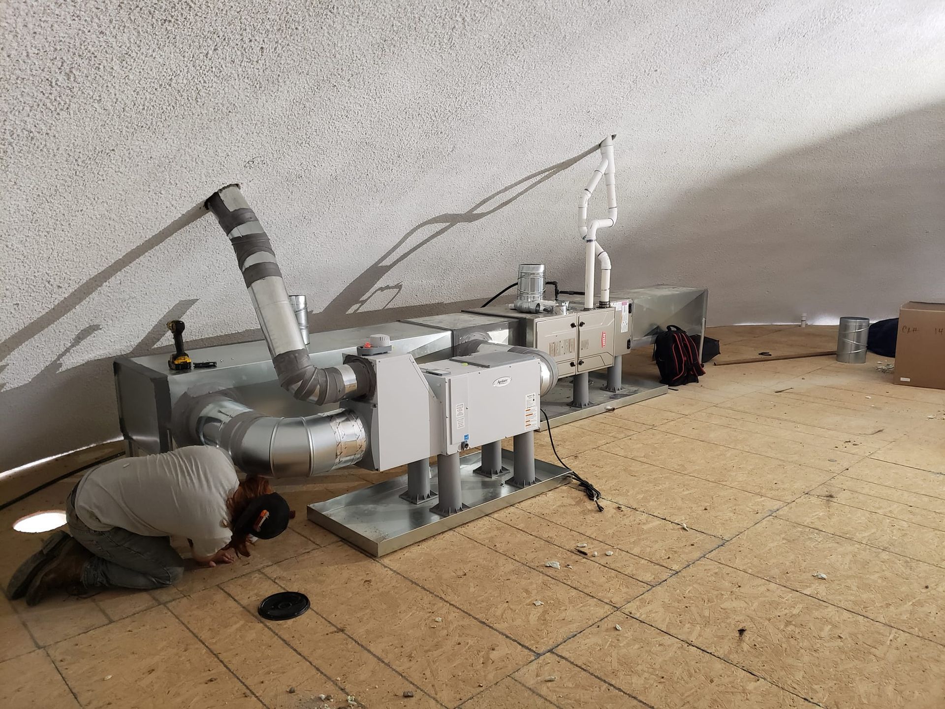 Person working on HVAC system in a dome-shaped room with wooden flooring.