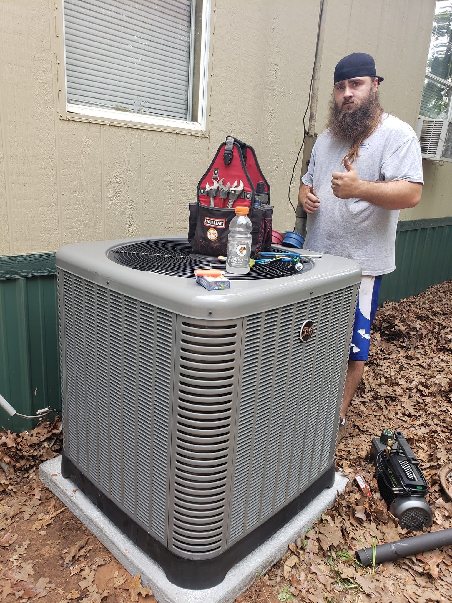Man with tools on AC unit outside a building, thumbs up.