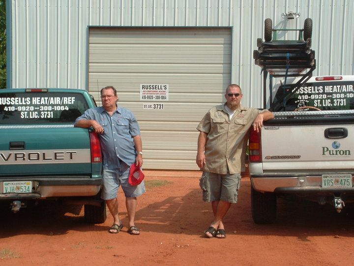 Two men leaning on pickup trucks in front of a building.
