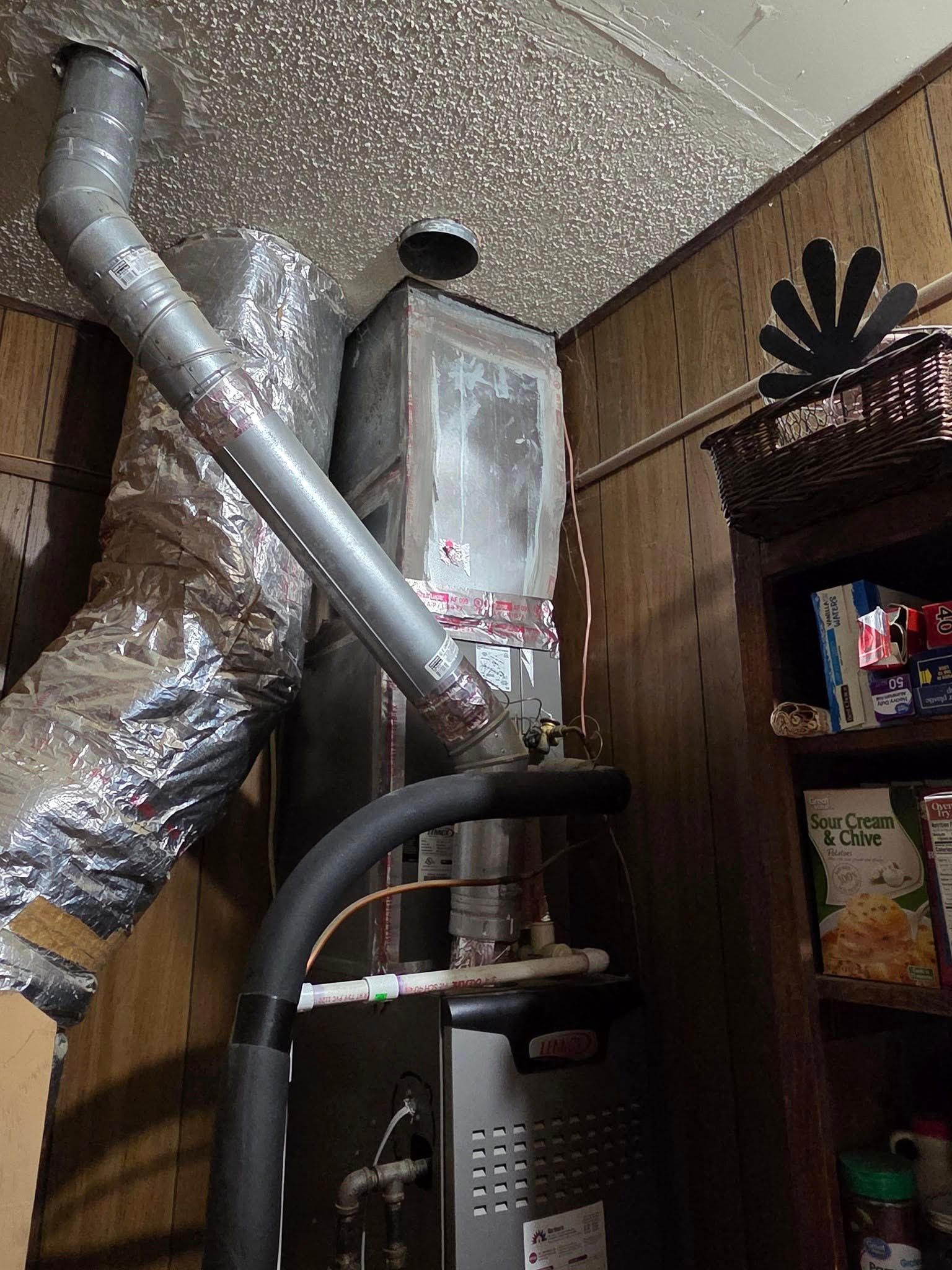 HVAC unit with ducts in a corner room with wood paneling and a basket shelf.