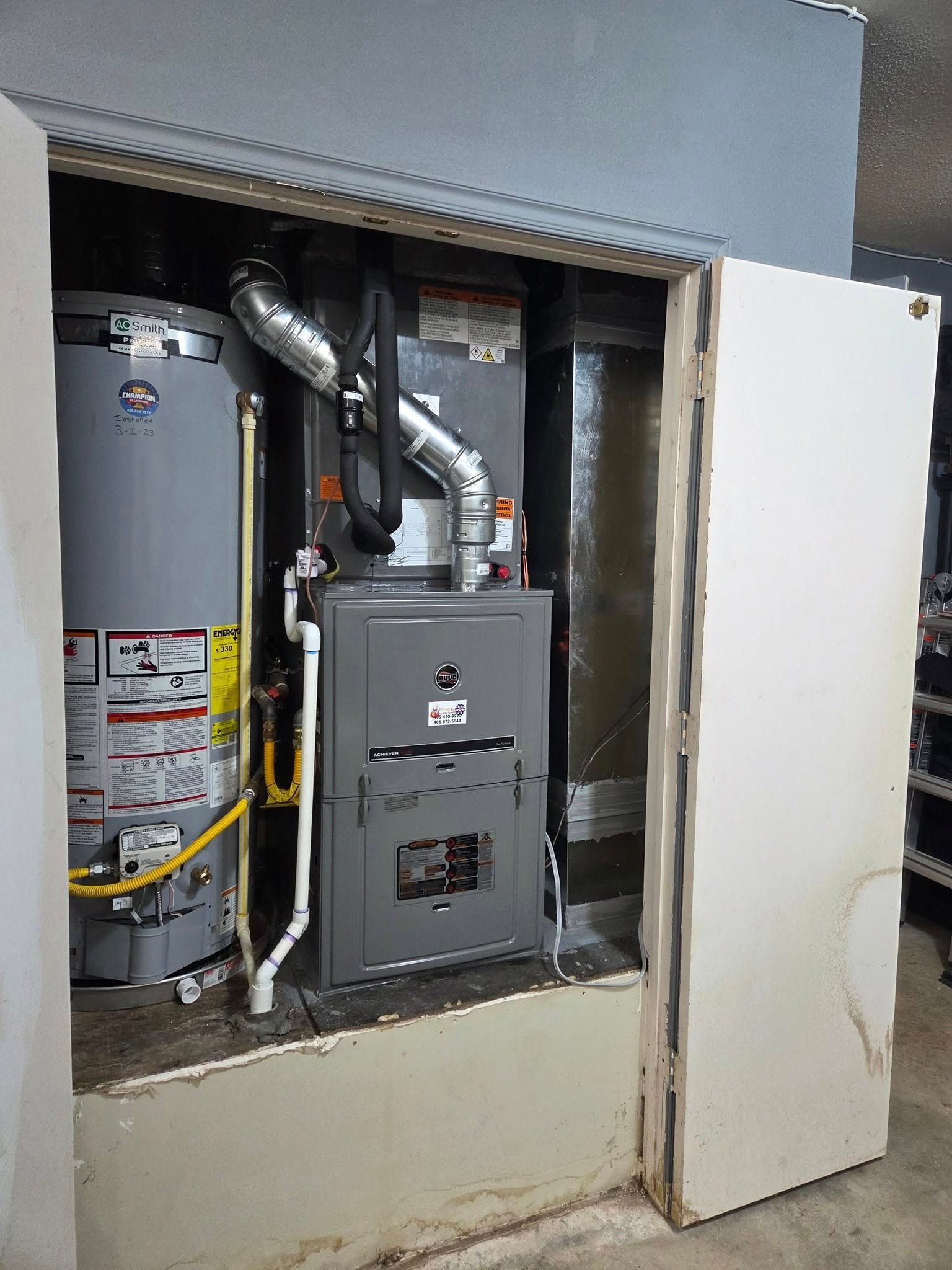 Furnace and water heater in a utility closet with a white door open.