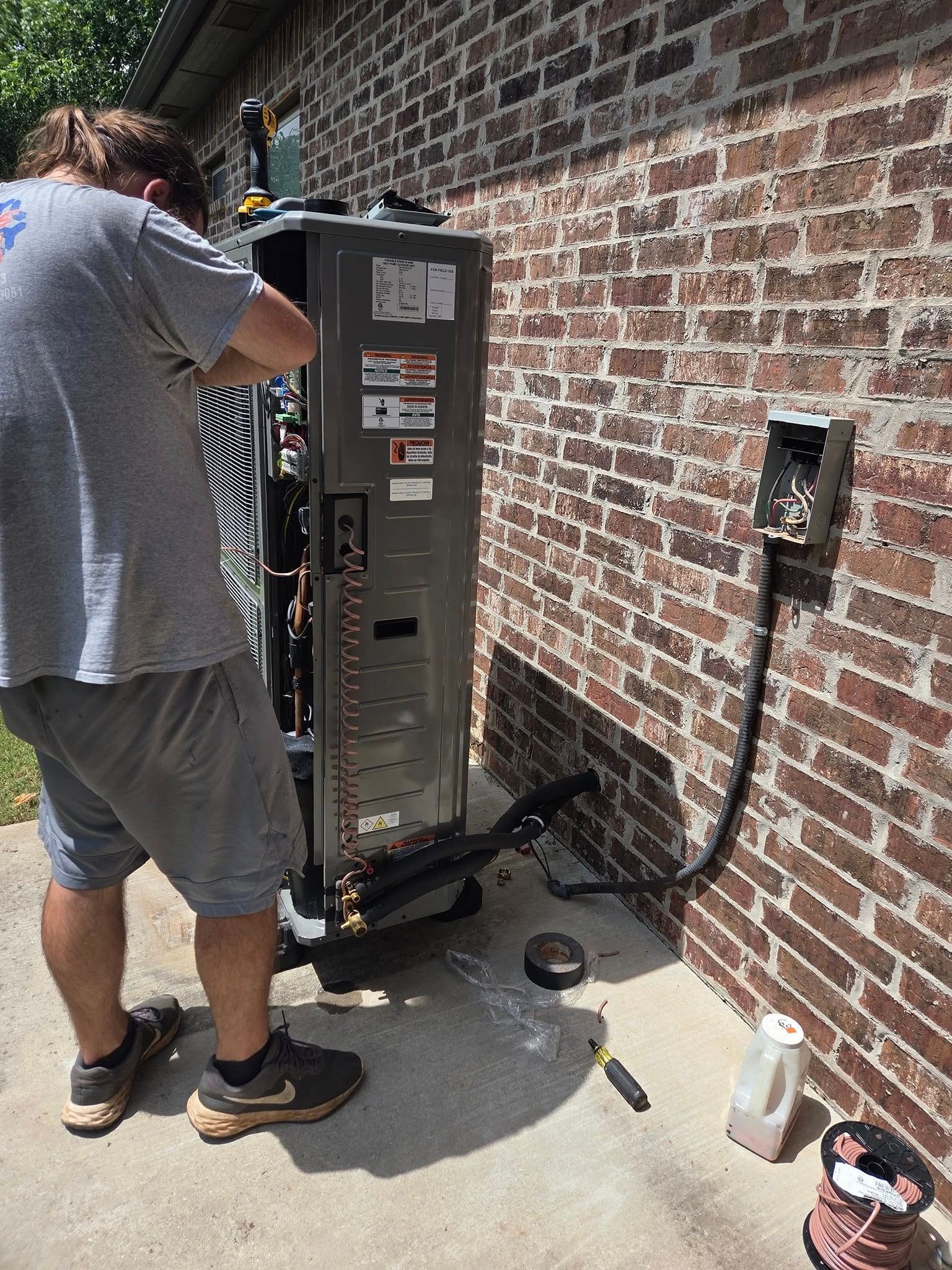 HVAC technician works on an outdoor air conditioning unit next to a brick wall.