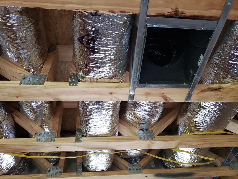 Interior view of an attic with silver ductwork running between wooden beams; a dark opening is visible.