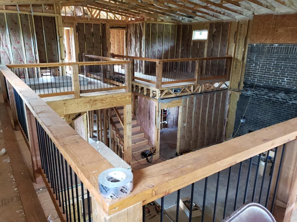 Interior of a house under construction; a second-story railing overlooks unfinished rooms and stairs.