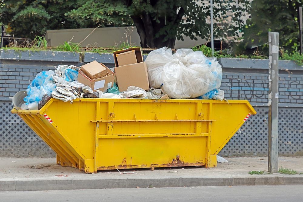 Yellow dumpster overflowing with trash on a sidewalk.