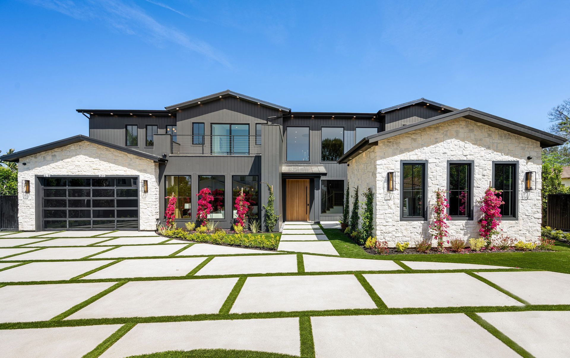 A modern two-story home featuring a combination of dark gray siding and light stone, with a large paved driveway.