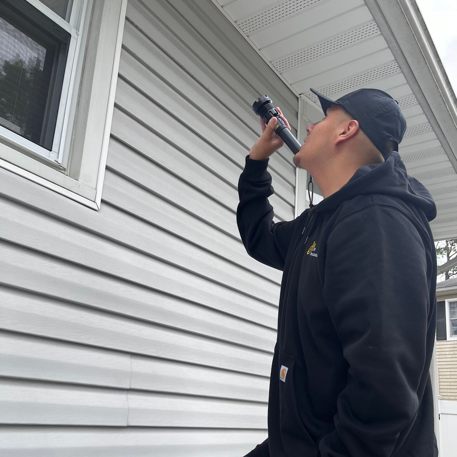Man in black hoodie drinking from a hose near a house.