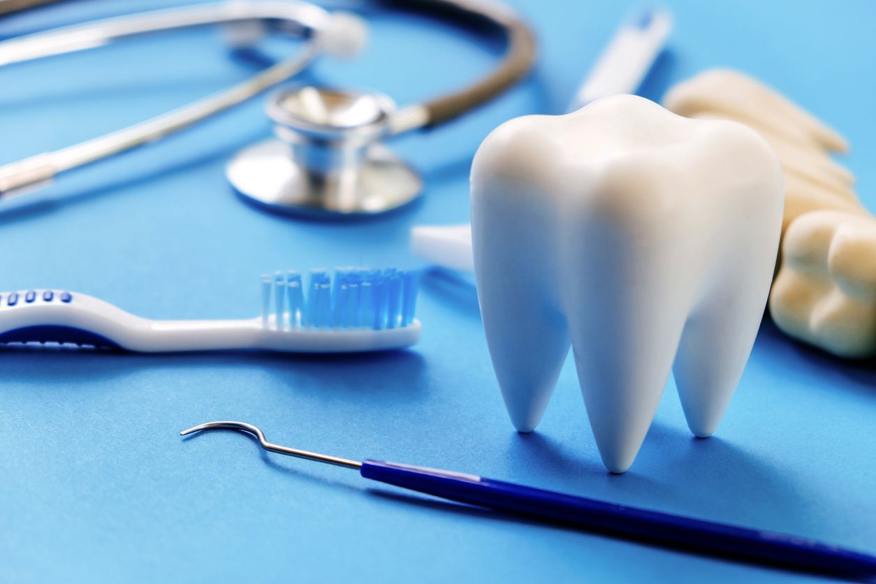 Dental tools and model tooth on a blue surface: stethoscope, brush, explorer.