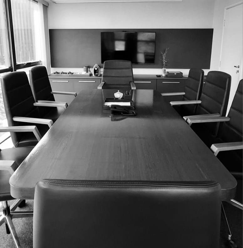 Uma foto em preto e branco de uma sala de conferências com uma mesa longa e cadeiras