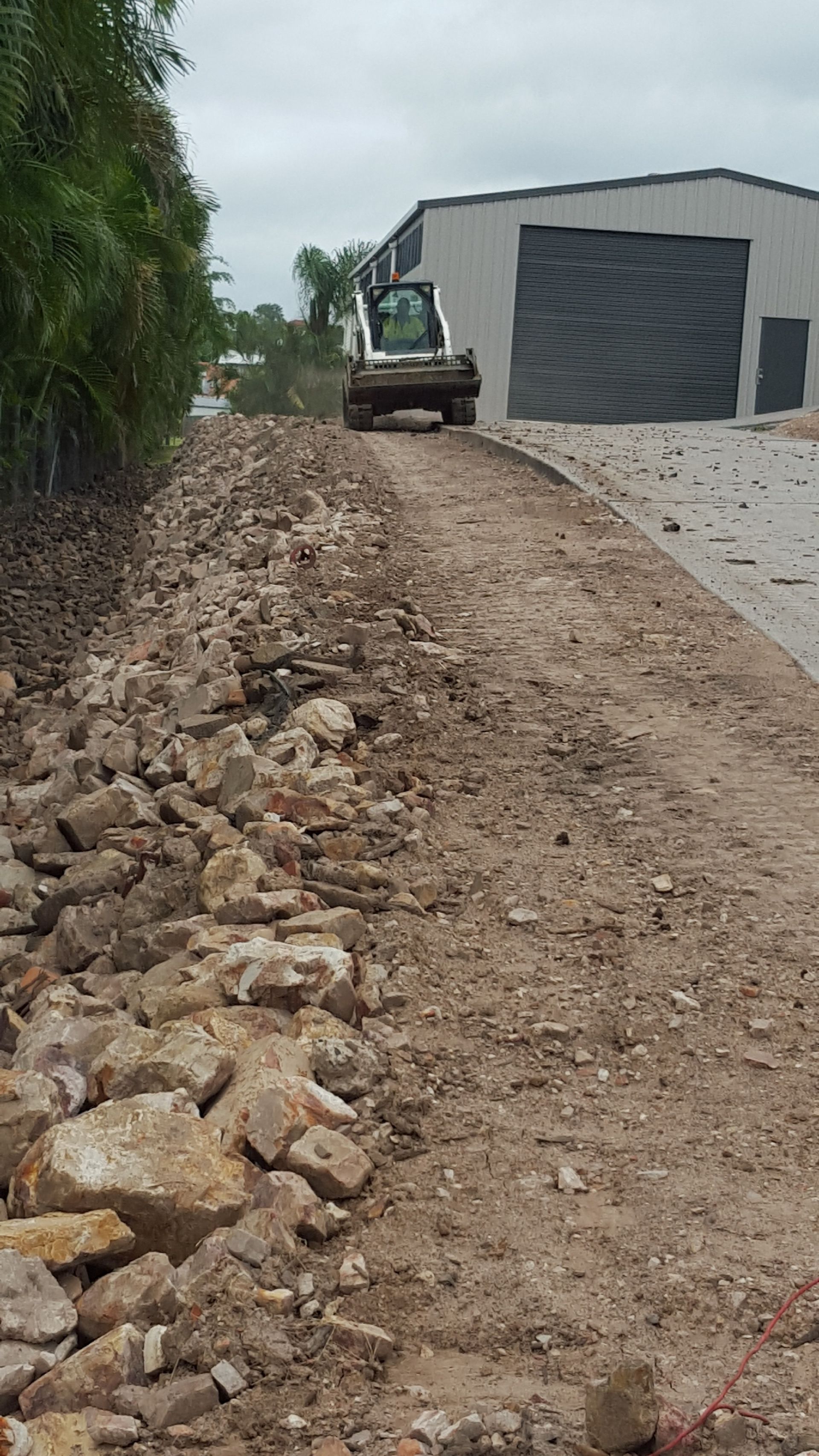 a Skid Steer on a Dirt Road, Next to a Pile of Rubble and a Building — Snell Earthworx In Craignish, QLD