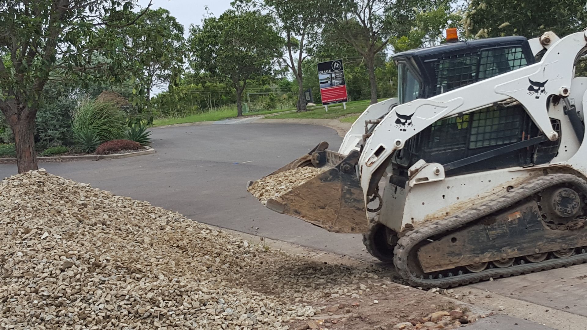 Bobcat skid steer loading stones onto asphalt driveway — Snell Earthworx In Craignish, QLD