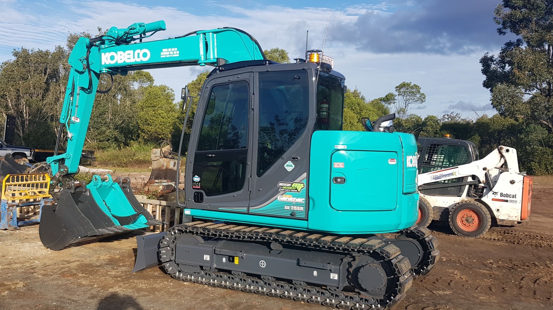 Green Kobelco Excavator with Black Tracks, Next to a White Bobcat on a Construction Site — Snell Earthworx In Craignish, QLD