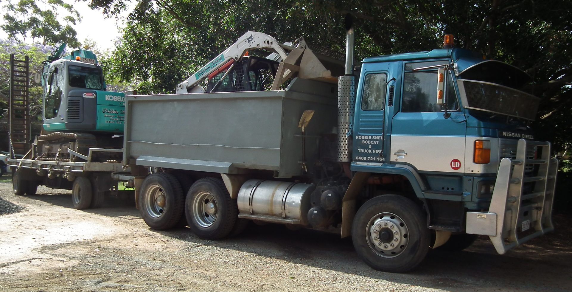 Blue and White Dump Truck with Excavator on a Trailer, Parked on a Dirt Road — Snell Earthworx In Craignish, QLD