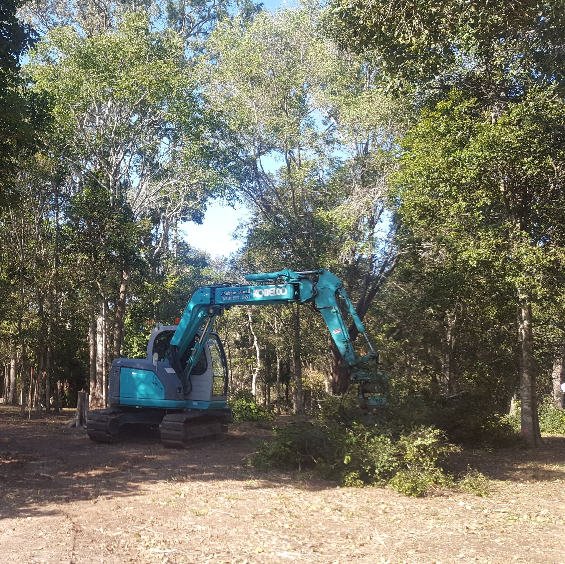 Blue Excavator Clearing Brush in a Wooded Area — Snell Earthworx In Maryborough, QLD