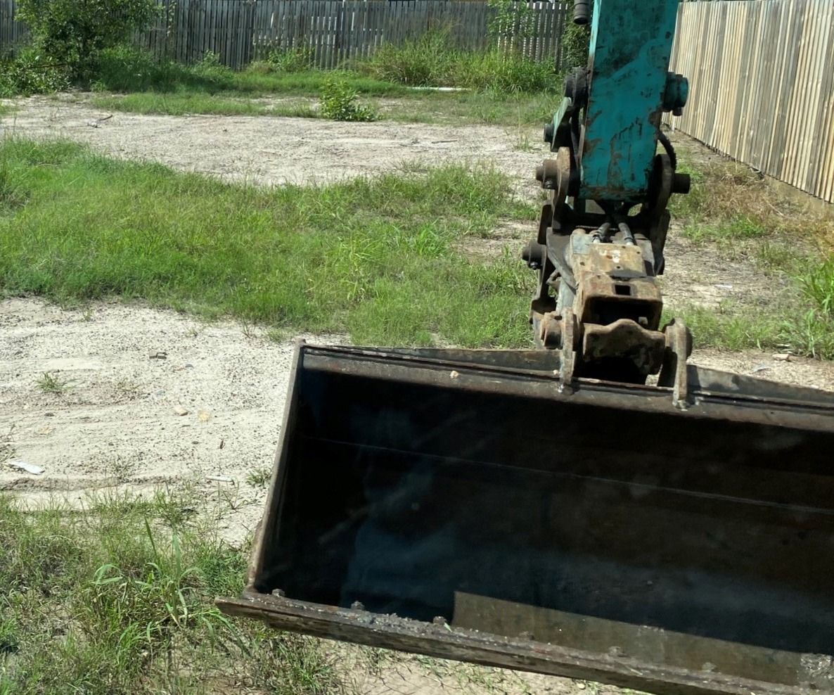 Bucket of a Teal Excavator Against a Grassy and Dirt Area — Snell Earthworx In Craignish, QLD