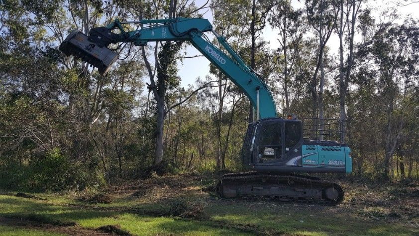 A Teal Excavator is Lifting Its Bucket in a Wooded Area — Snell Earthworx In Craignish, QLD