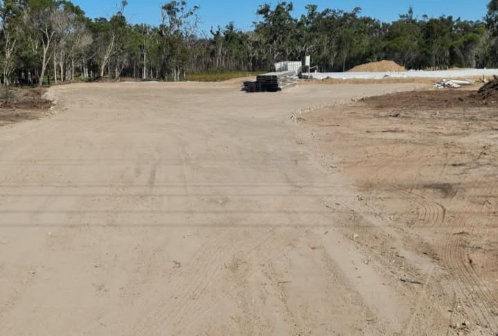 Dirt road leading to a cleared area with construction materials and trees under a blue sky. — Snell Earthworx In Hervey Bay, QLD