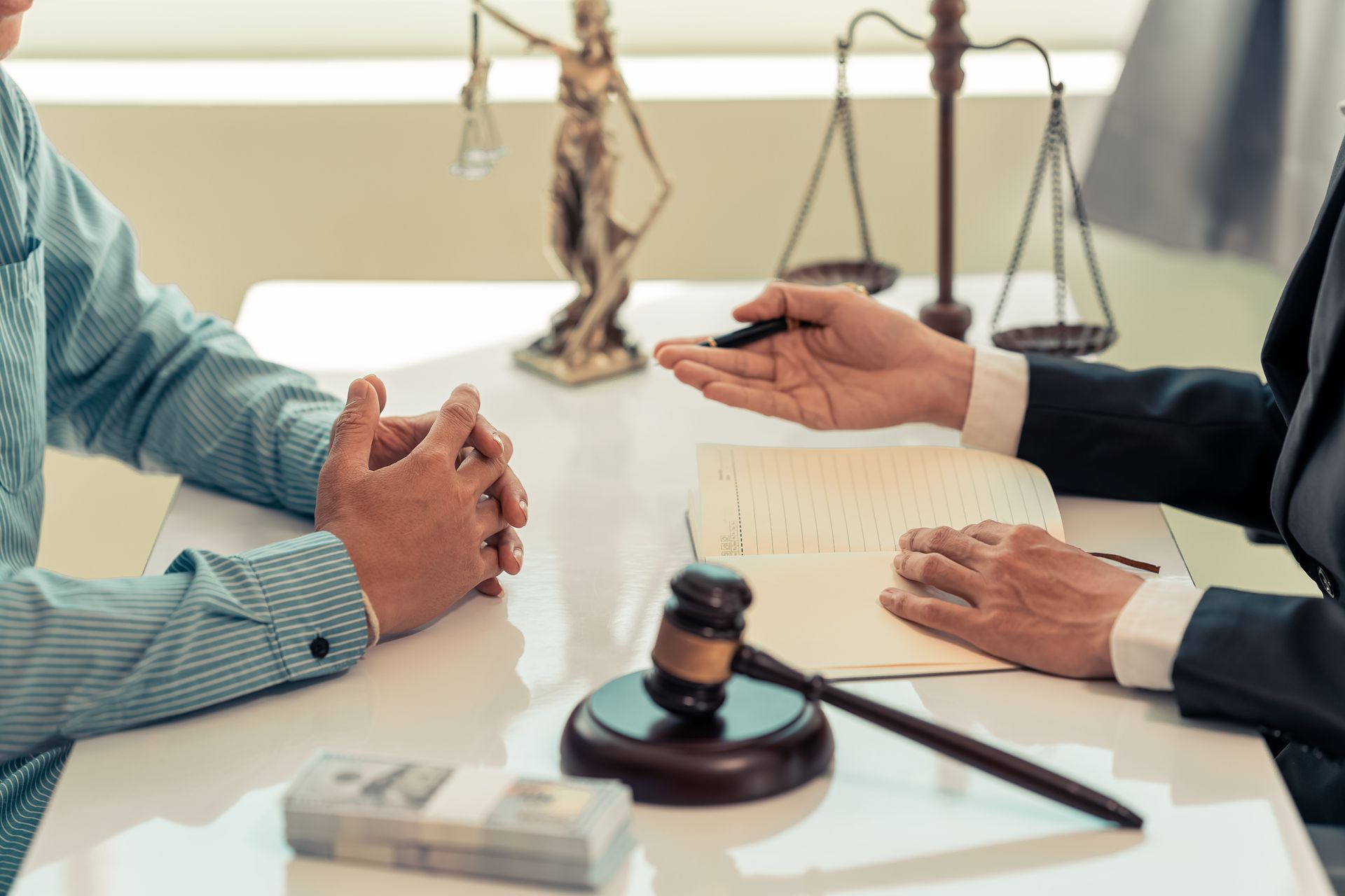 Two people in a law office discussing a case across a desk with a gavel and legal papers. Two people in a law office discussing a case across a desk with a gavel and legal papers.