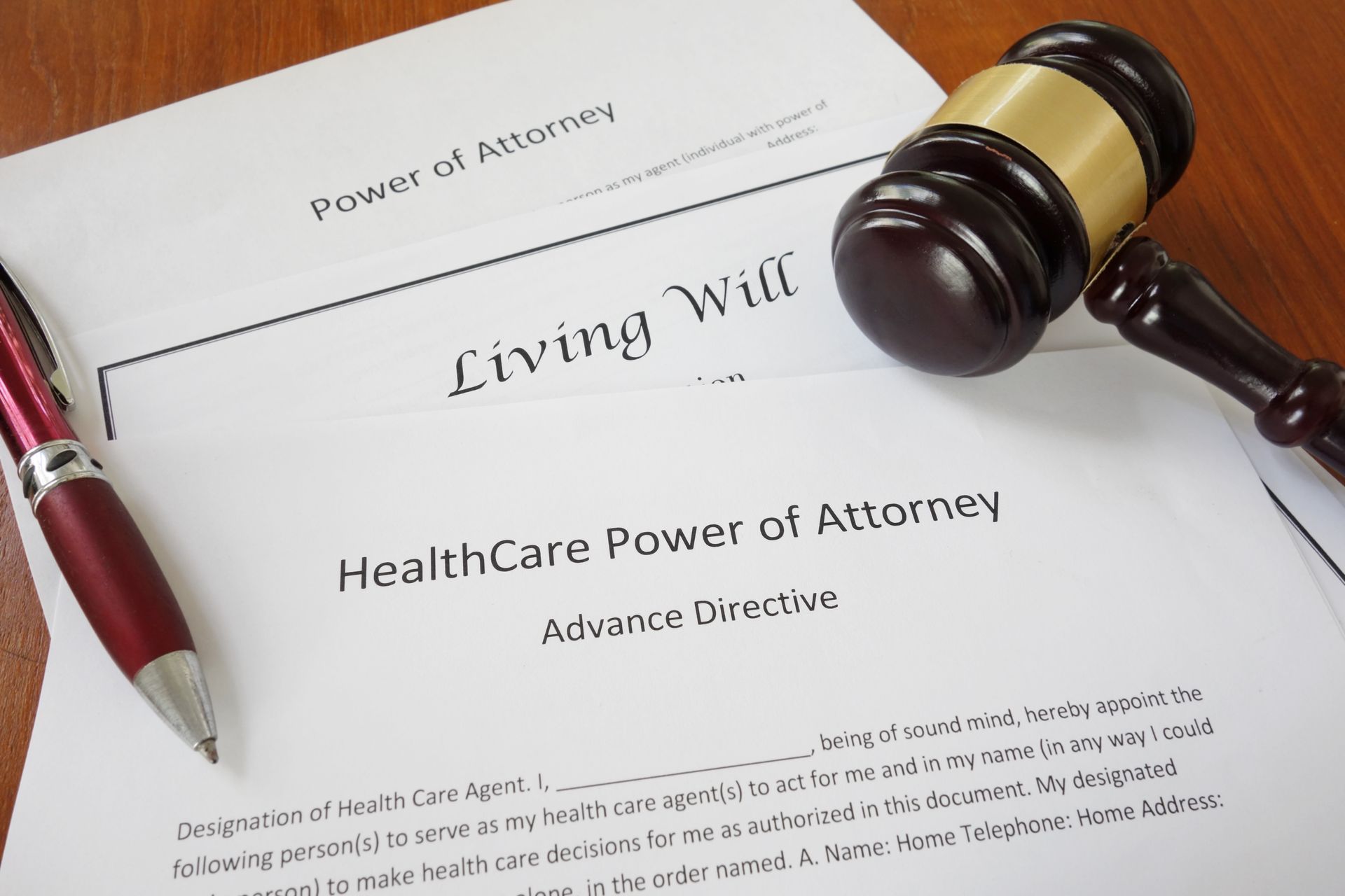 A gavel, a red pen, and legal forms for a Power of Attorney, Living Will, and Healthcare Power of Attorney on a desk.