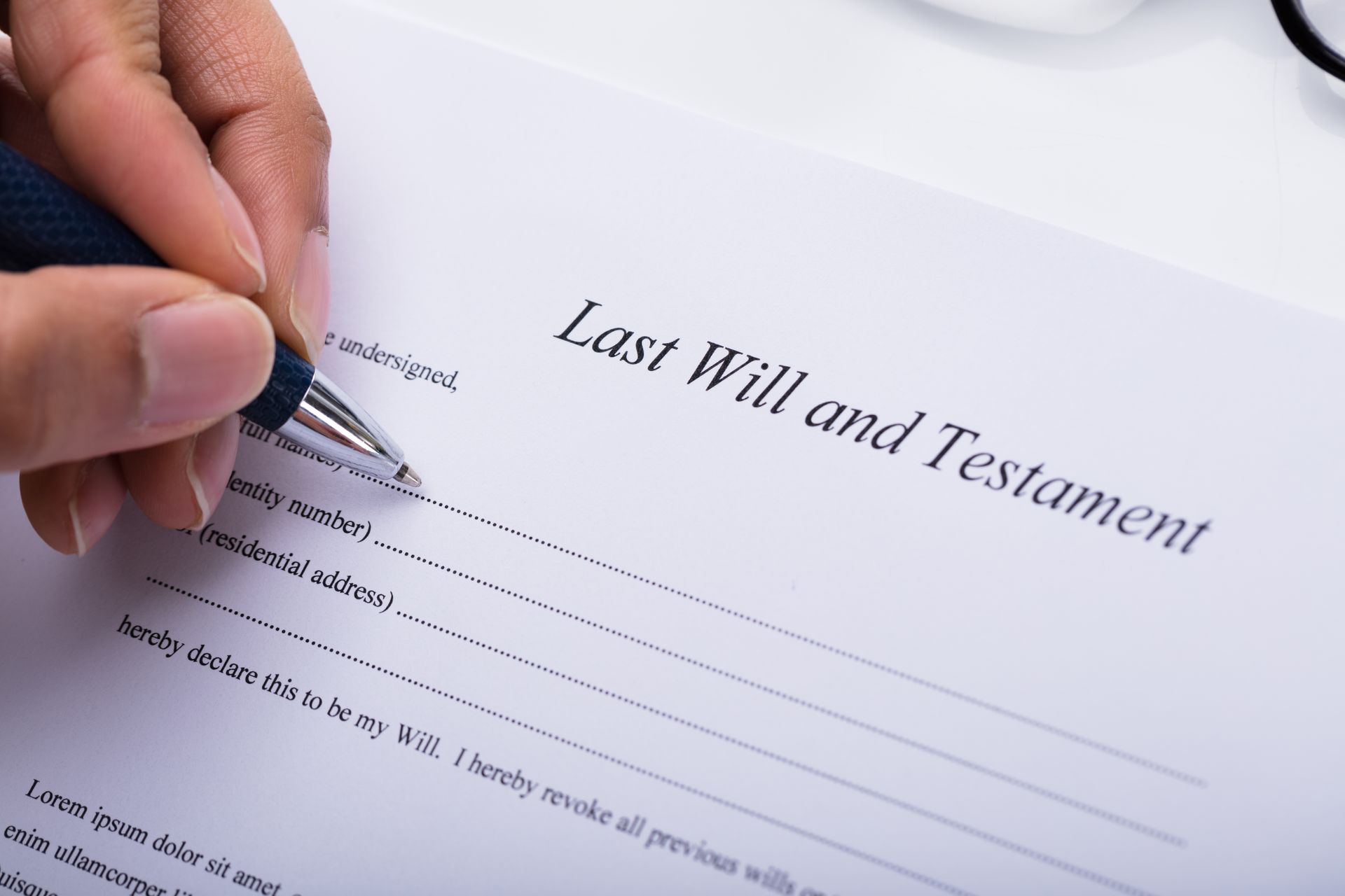 A person's hand uses a pen to fill out a legal document titled Last Will and Testament.