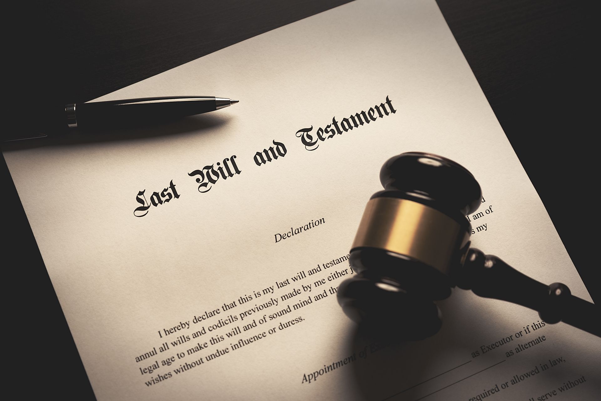 A wooden gavel and a fountain pen rest on top of a legal document titled Last Will and Testament.