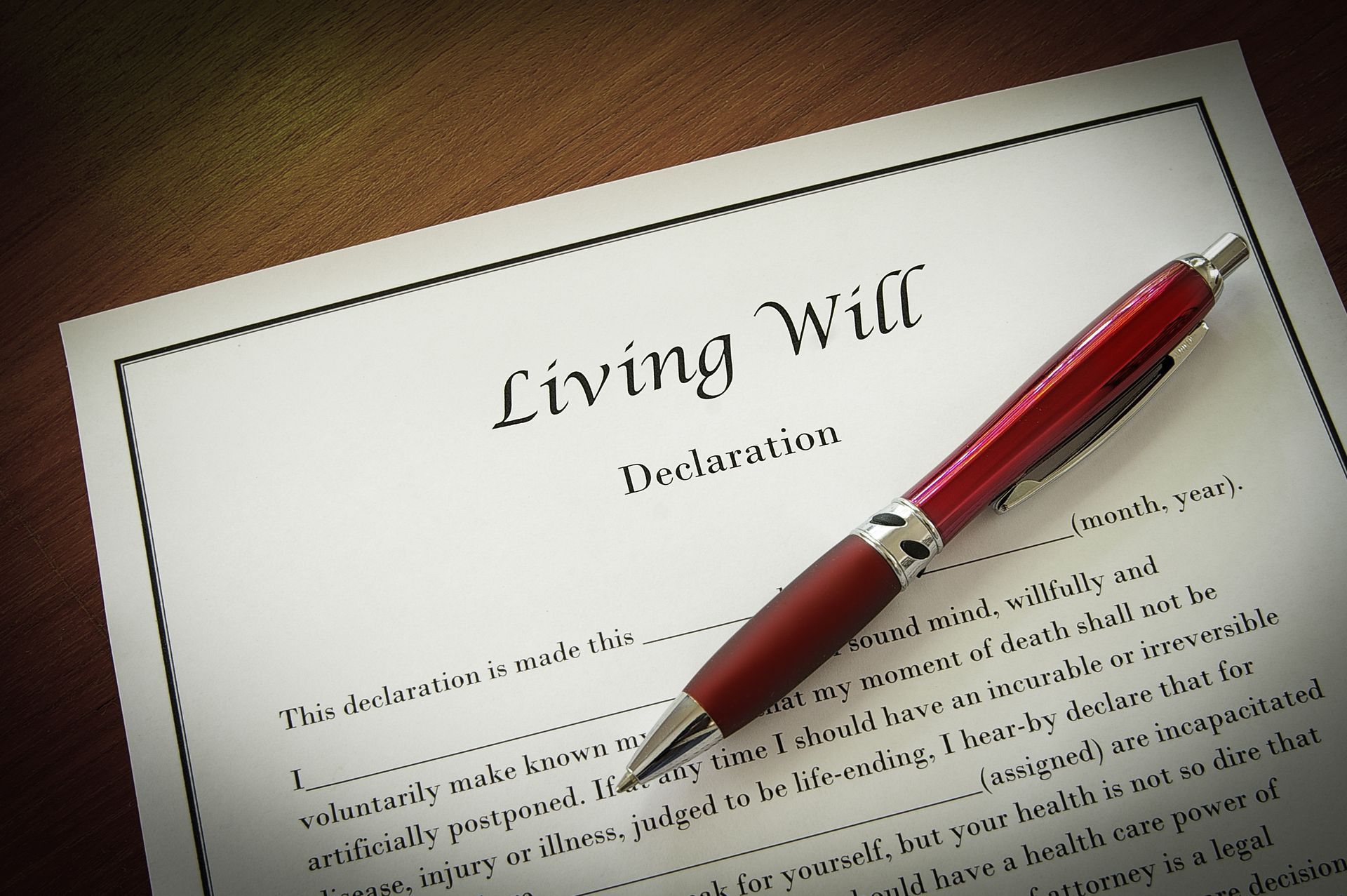 A red pen rests on a document titled Living Will on a dark wooden surface.