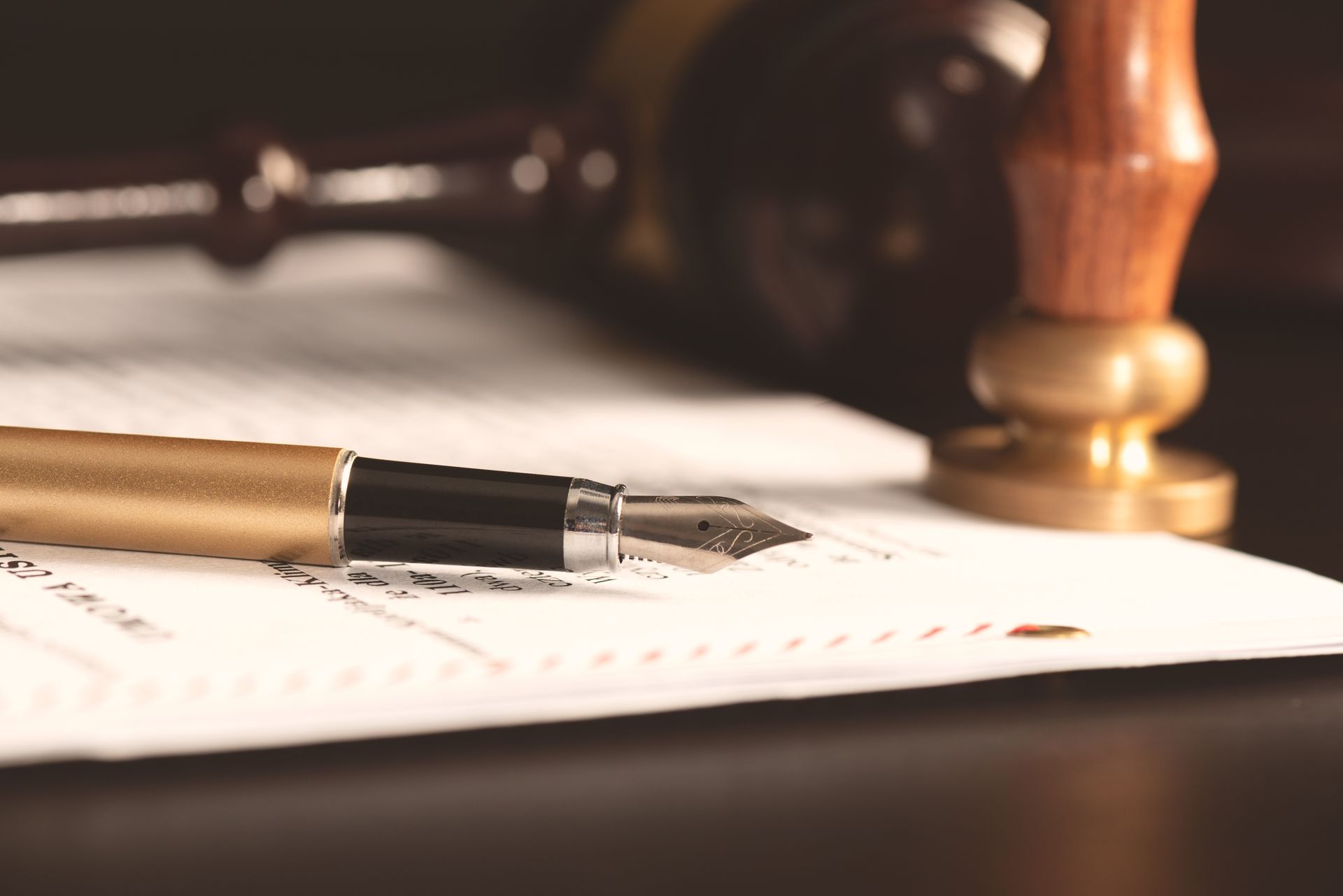 A gold fountain pen rests on a document next to a wooden gavel and stamp in a law-themed setting.