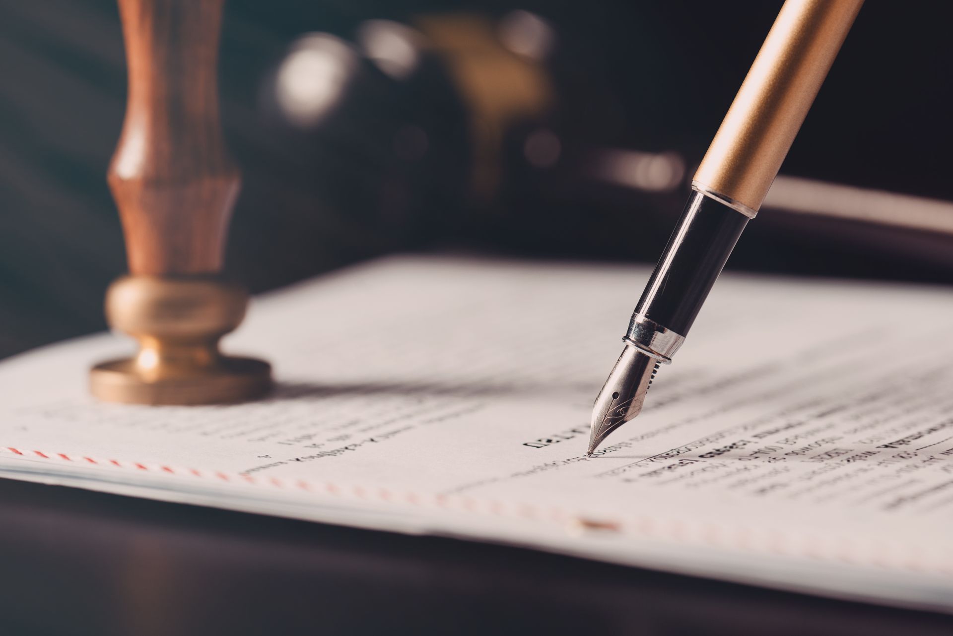 A fountain pen writes on a legal document beside a wooden wax seal stamper on a desk. A fountain pen writes on a legal document beside a wooden wax seal stamper on a desk.