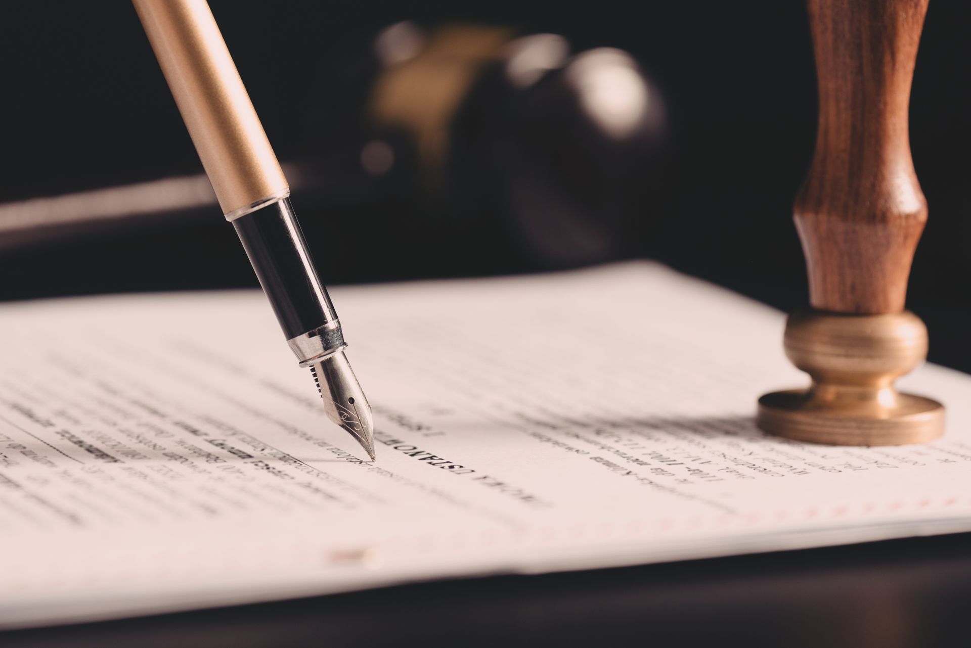 A fountain pen writes on a document next to a wooden notary seal against a dark background.