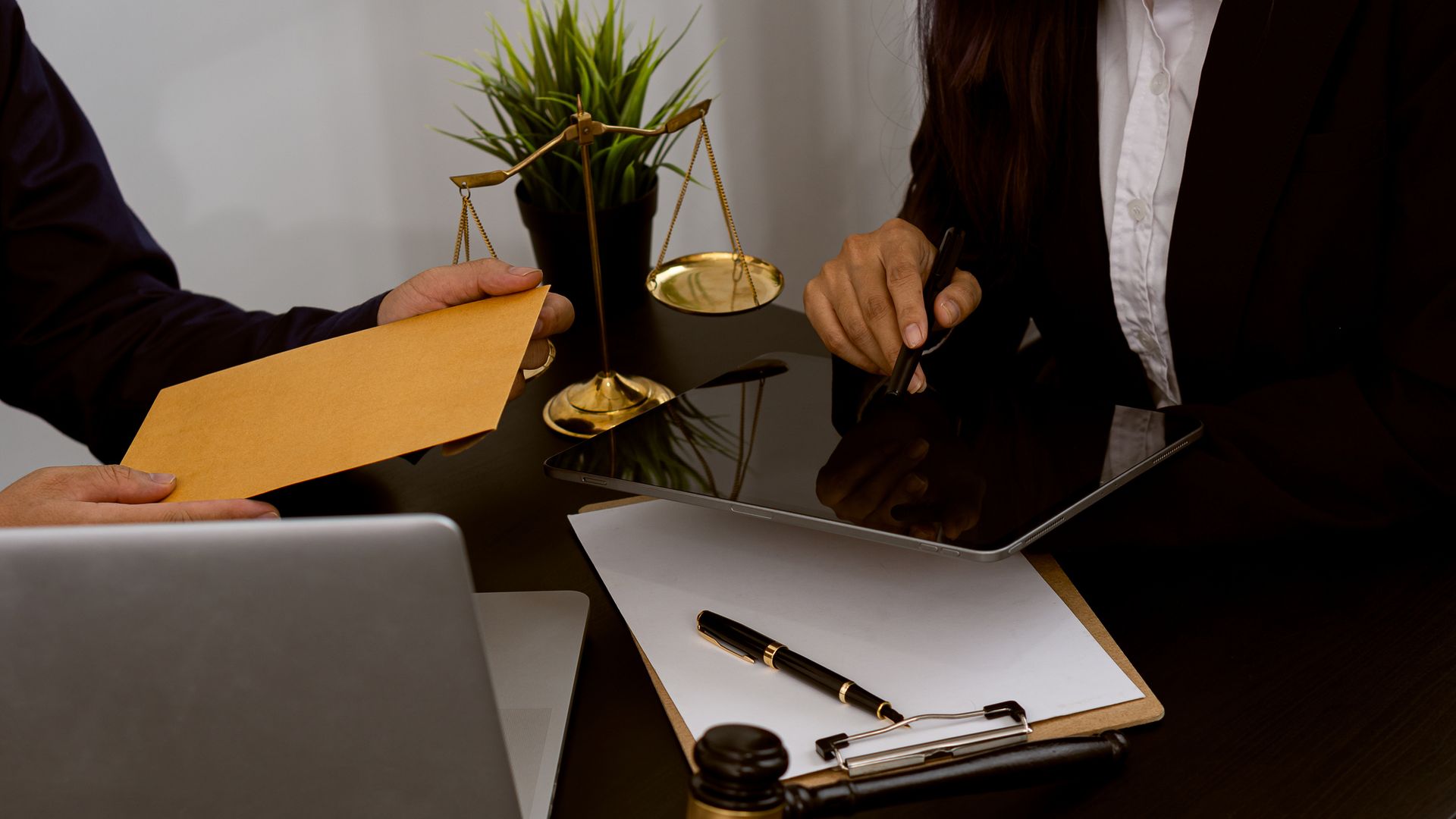 Lawyer consulting client with legal documents, scales of justice, and gavel on desk.