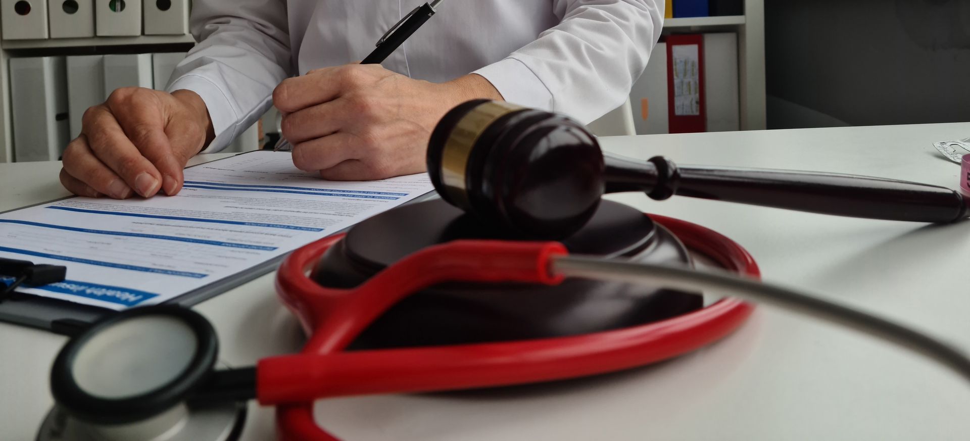 Doctor writing on clipboard with stethoscope and gavel on desk, medical legal concept.