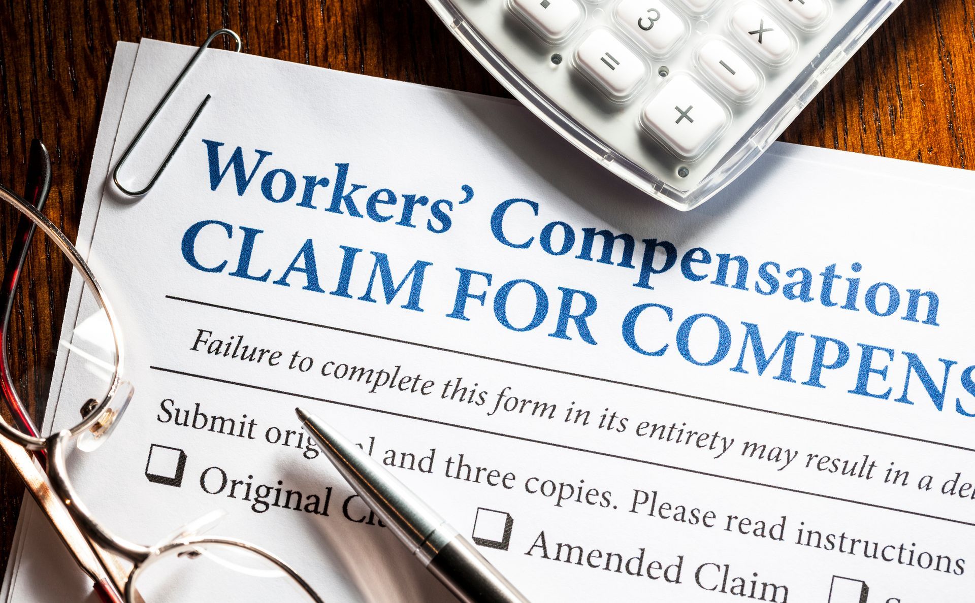 Close-up of a workers' compensation claim, with a pen, a pair of glasses and a calculator on top.