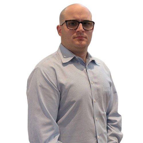 A bald man with glasses wearing a light blue button-down shirt, standing against a white background.