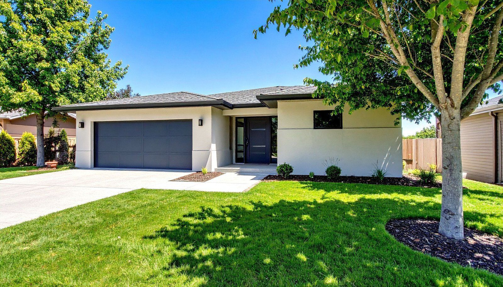 Modern house with a gray garage door, bright green lawn, and a blue sky.