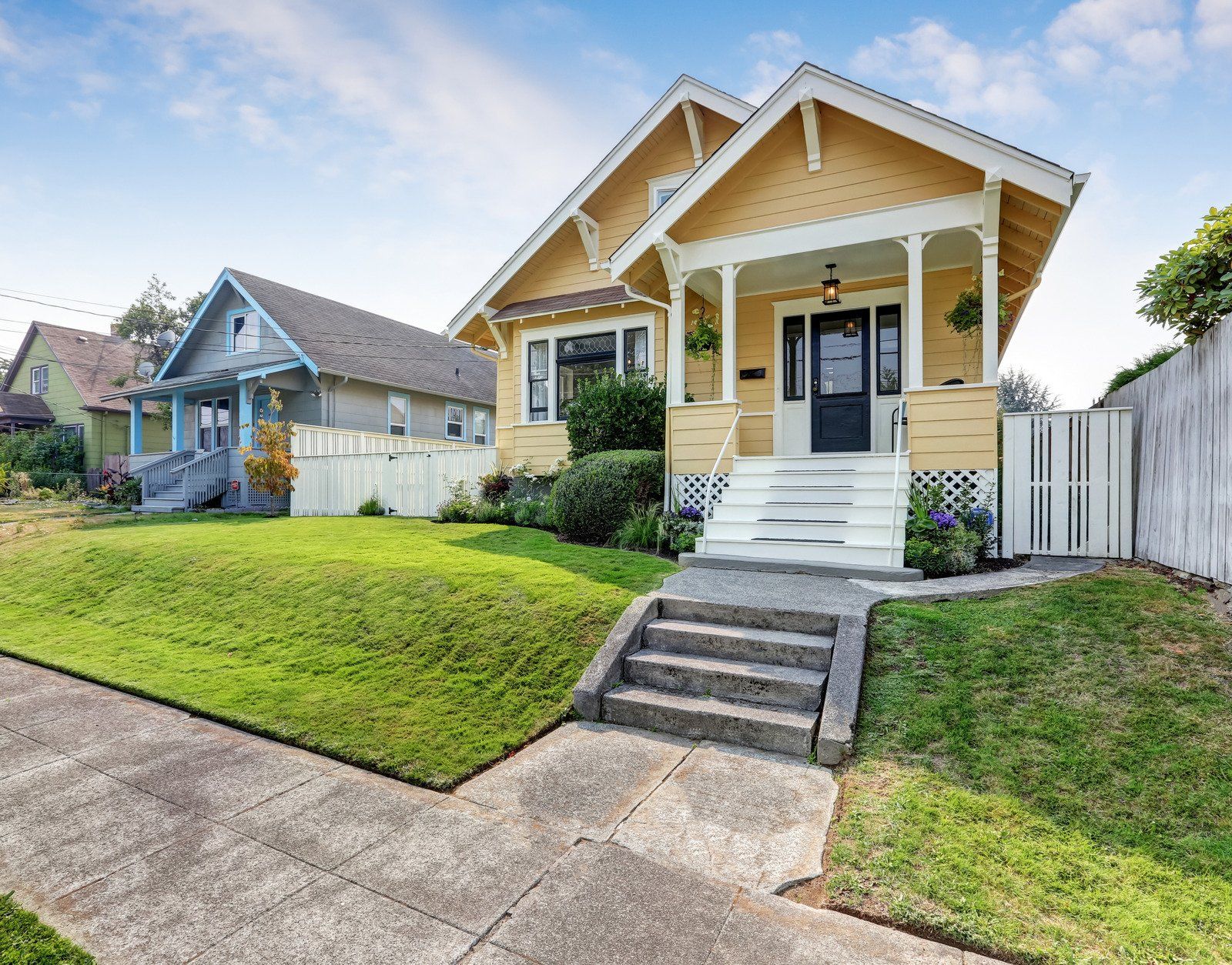 Yellow Craftsman house with white porch and steps, on a grassy hillside.