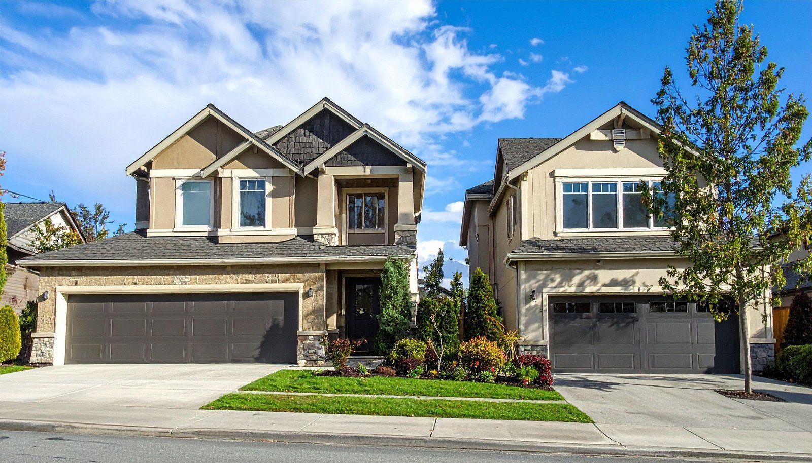 Two-story houses with brown garage doors sit side by side under a blue sky, on a street.