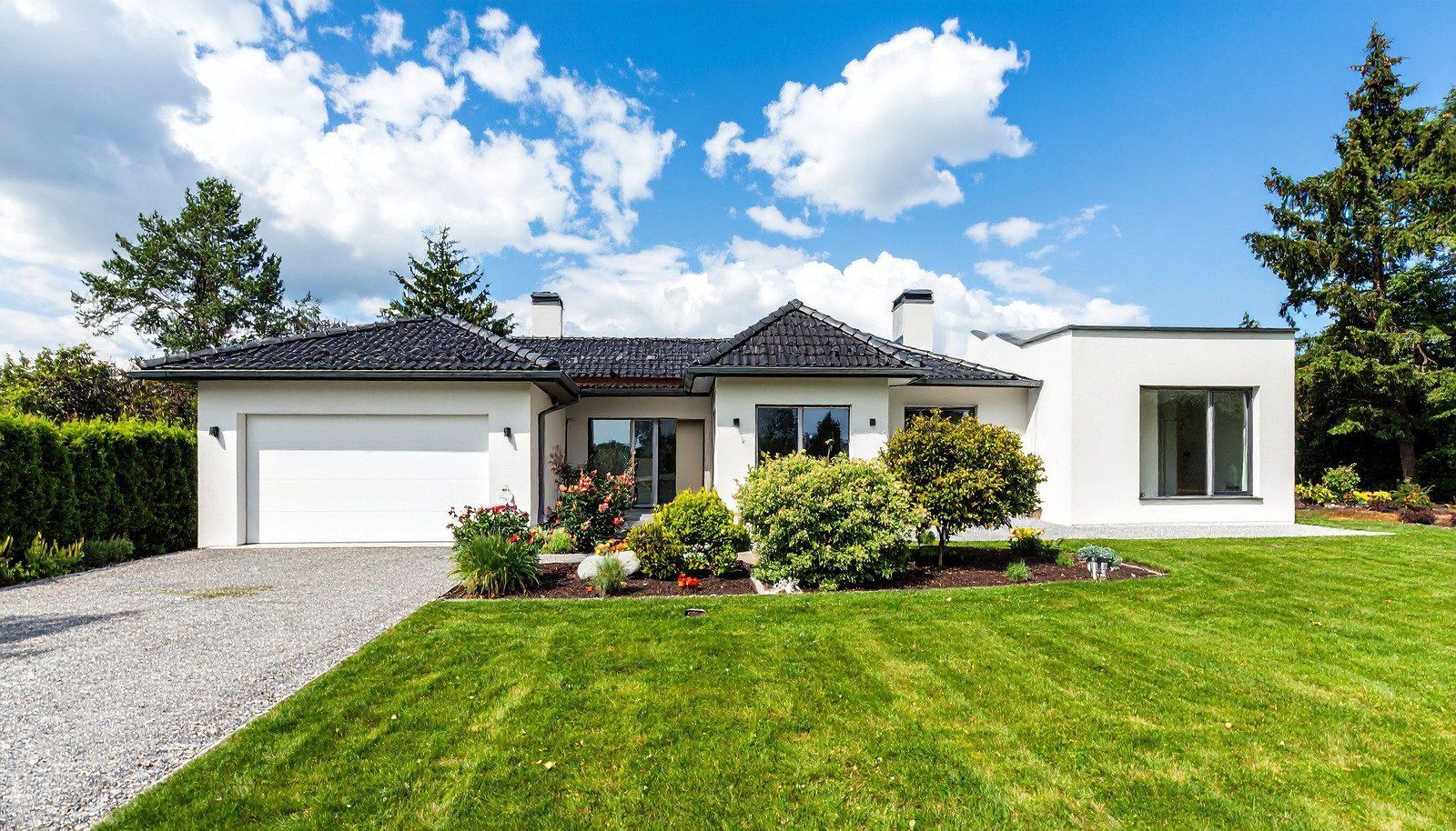 White house with black roof and attached garage, lush green lawn, sunny day.