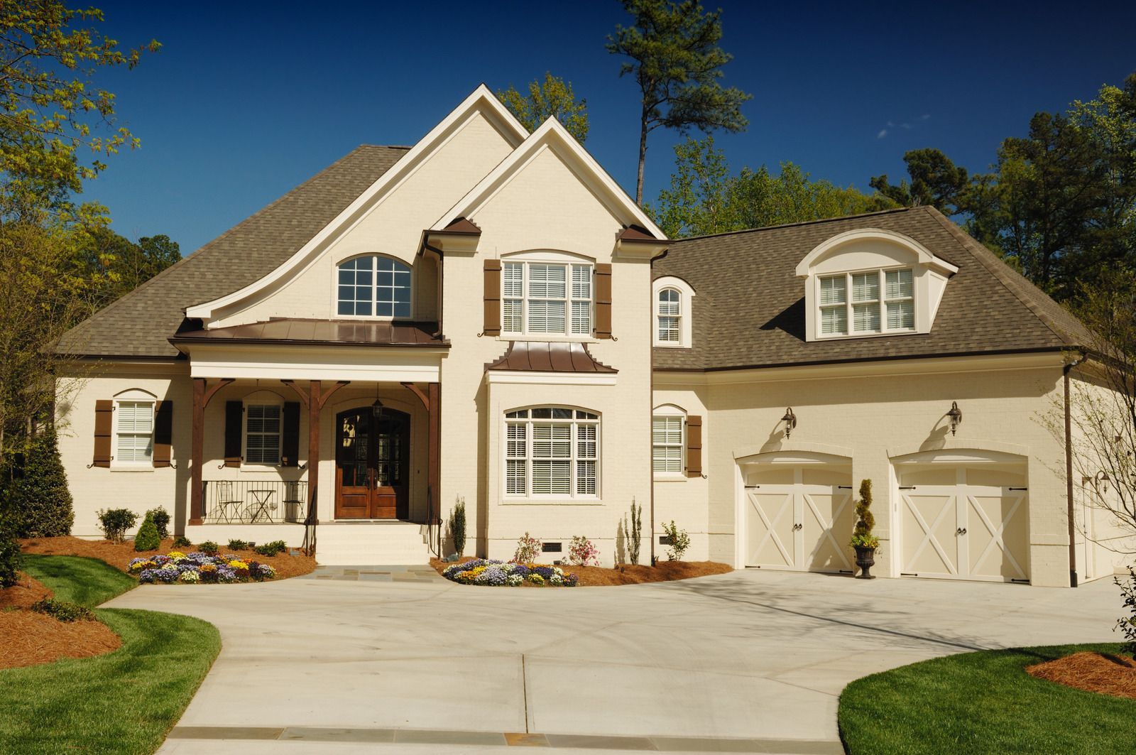 Beige two-story house with brown shutters and a two-car garage under a blue sky.