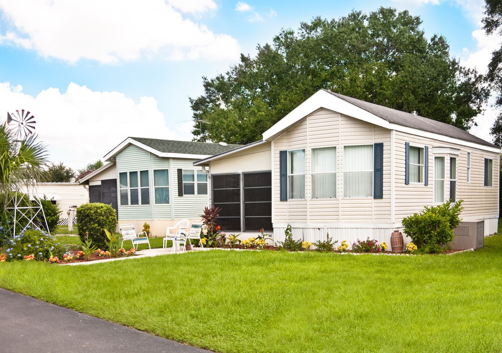 Two mobile homes with green lawns and flower beds under a blue sky.