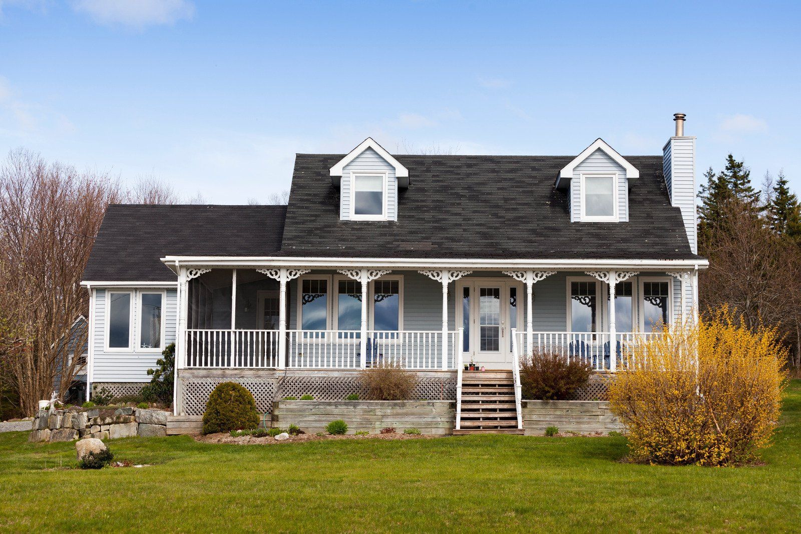 Light blue house with white trim, porch, and dormers under a blue sky.