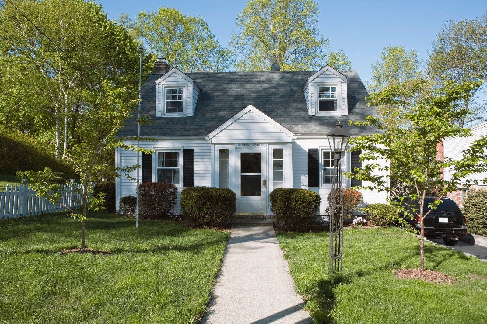 White house with gray roof, dormers, and sidewalk leading to the front door; green lawn and trees.