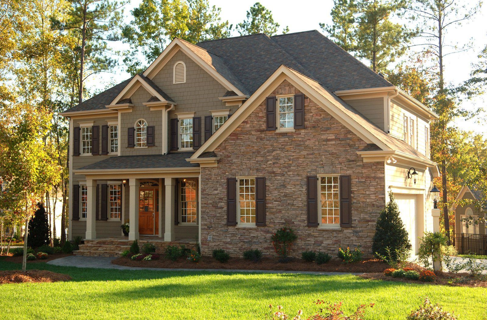 Two-story house with stone and gray siding, brown shutters, and a well-manicured lawn.