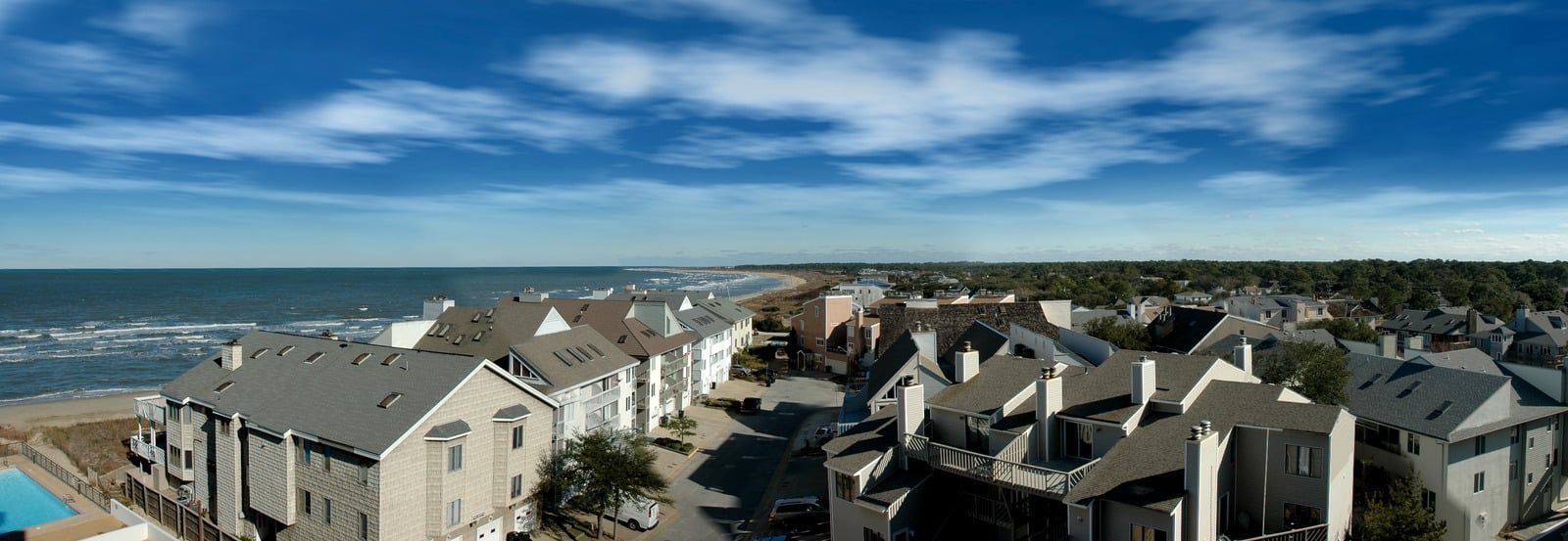 Aerial view of a coastal neighborhood, with houses near a beach and ocean under a blue sky.