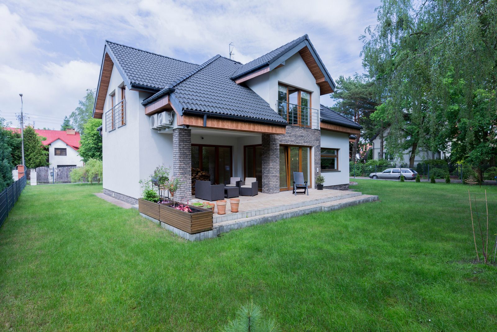 Two-story house with a black roof, stone accents, and a patio on a green lawn.