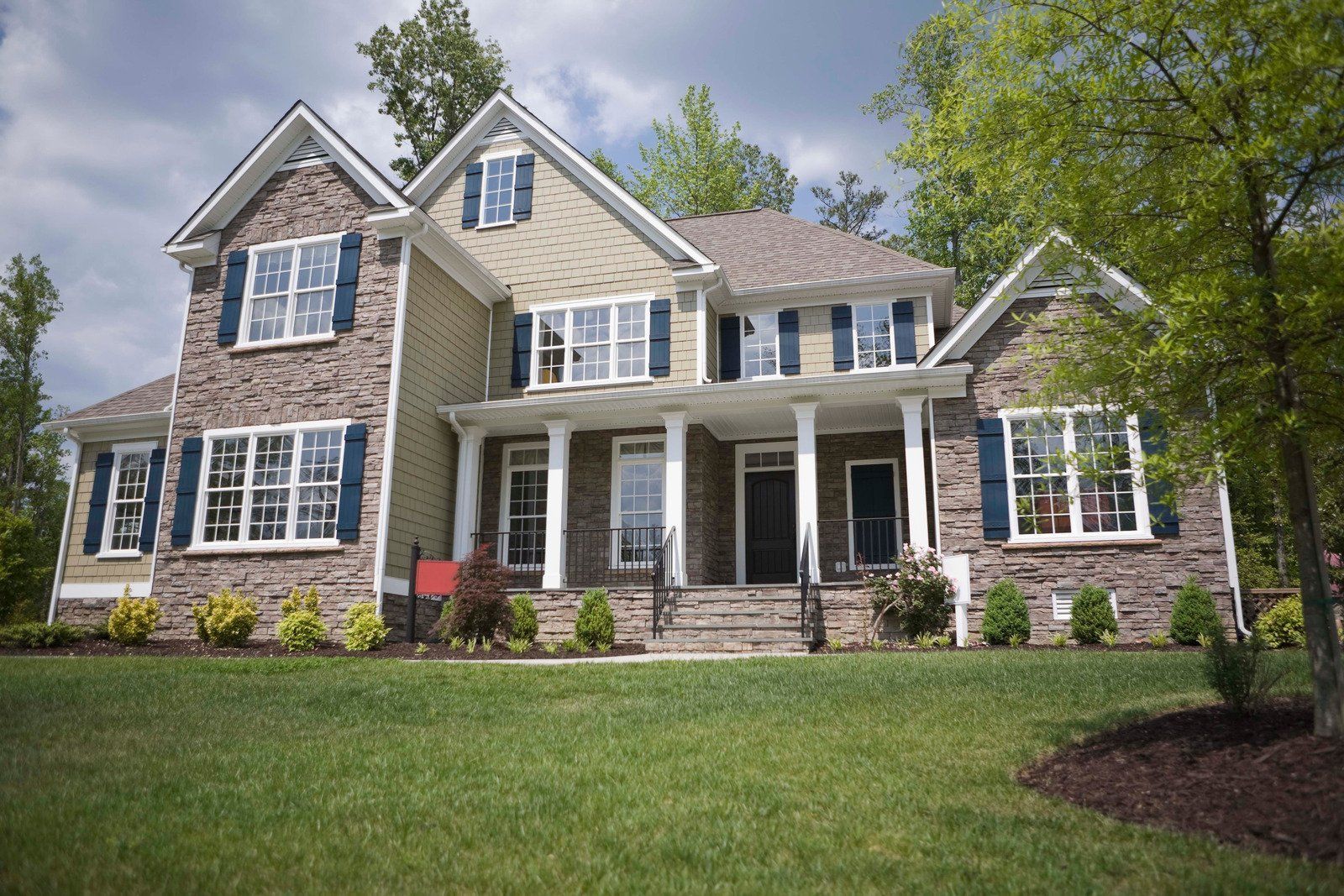 Two-story house with stone and tan siding, blue shutters, and a green lawn.